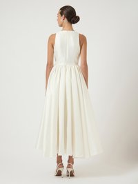 Ένα αμάνικο, μακρύ φόρεμα από σατέν στα χρώματα του ελεφαντόδοντου με εφαρμοστό τοπ, πλισέ φούστα και διακριτικό φερμουάρ στην πλάτη.