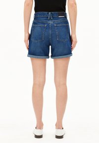 Shorts en denim de couleur bleu foncé avec ourlets roulés, dotés d'une taille haute, de poches arrière classiques et d'un logo sur la ceinture.