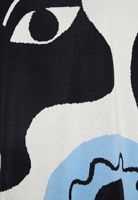 Tessuto a maglia con un design grafico nei colori nero, bianco e azzurro chiaro. Le forme astratte includono grandi occhi e contorni fluidi.