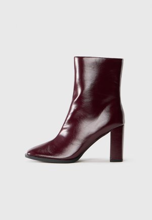 Shiny dark burgundy mid-calf leather boot with pointed toe and block high heel on neutral background.