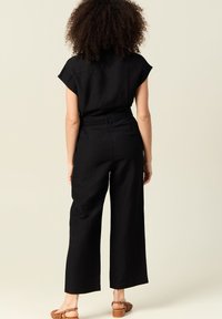 Svart linne jumpsuit med korta kappramar, en figursydd midja och vida byxor. Har en slät textur och minimal design.