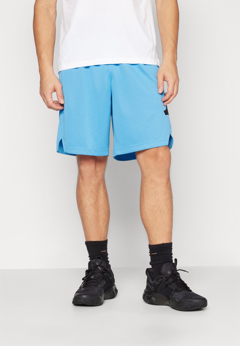 Moške lahke modre mrežaste športne hlače s stranskimi razporki, v kombinaciji s črnimi teniskami in črnimi kratkimi nogavicami. Tkanina ima rahlo sijajno površino.