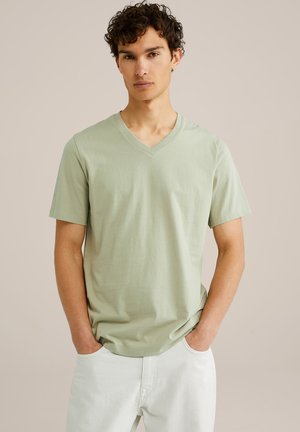 Camiseta verde claro de manga corta y cuello en V, confeccionada en tela suave, combinada con pantalones de color claro, mostrando un ajuste relajado y un diseño sencillo.