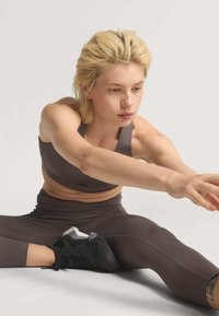 Dunkelgraues sportliches Crop-Top und hoch taillierte Leggings aus glattem, elastischem Stoff. Schwarze Schuhe mit hellen Akzenten. Person dehnt sich nach vorne.