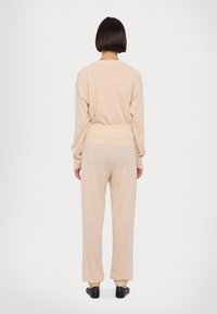 Svetlo bež komplet za prosti čas, ki vključuje sproščen, dolg rokav top in tapered hlače z elastičnimi manšeti. Mehka, teksturirana tkanina na obeh kosih.