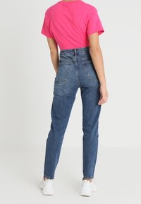 Höga blå jeans med rak passform, bakfickor och en lätt blekt textur, kombinerat med en ljusrosa t-shirt och vita sneakers.