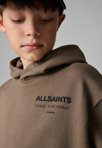 Smeđa pamučna dukserica s kapuljačom s vezicom i izvezenim "ALLSAINTS" u crnoj boji na prsima. Glatka tekstura s opuštenim krojem.