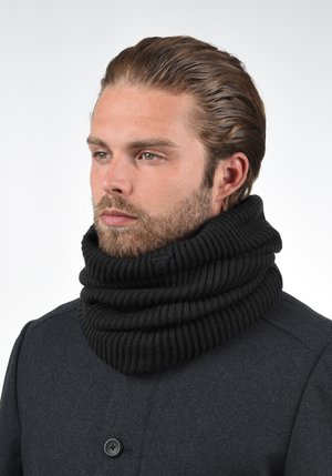 Black ribbed knit scarf, thick and bulky, wrapped around the neck. Model wears a dark coat with visible button details.