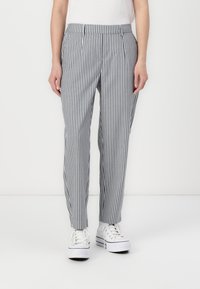 Randiga byxor i grått och vitt, med en avslappnad passform, platt framsida och sidofickor, kombinerade med vita sneakers.