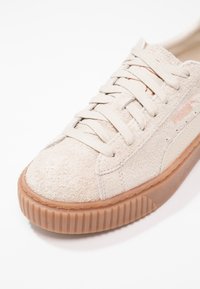 Baskets en daim beige clair avec semelle épaisse en gomme, fermeture à lacets et logo PUMA sur le côté et la languette, vues en gros plan sous un angle frontal.