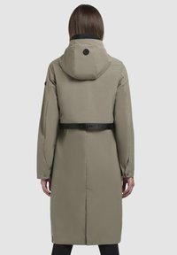 Palton lung de culoare khaki cu glugă, având un guler negru și un cordon ajustabil. Textură netedă cu detalii cu nasturi pe mâneci.