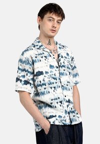 Camicia a maniche corte con bottoni di colore bianco e motivo a macchie blu, realizzata in tessuto leggero, con una vestibilità comoda e un design colletto.