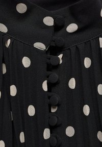 Tissu noir avec de gros pois blancs et une rangée de boutons noirs recouverts de tissu au centre.