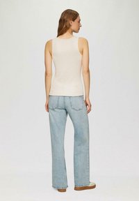 Beige ärmelloses Oberteil aus weichem Stoff, kombiniert mit hellen, weit geschnittenen Jeans. Die Jeans haben einen klassischen Schnitt und dezente Nähdetails.