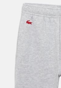 Calças de moletom cinza claro com cintura elástica e um pequeno logótipo de crocodilo vermelho na parte superior da coxa esquerda.