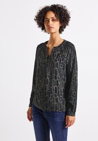 Blouse à manches longues noir et doré avec un col en V et une coupe ample, présentant un design géométrique abstrait et des manches à poignets.
