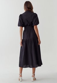 Zwarte midi-jurk met poffende mouwen, getailleerde taille en gelaagde rok. Gemaakt van lichtgewicht materiaal, met een gladde, matte textuur.