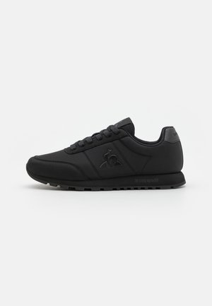 Black athletic shoes with a smooth synthetic upper, lace-up design, logo on the side, and textured rubber sole. Classic silhouette.