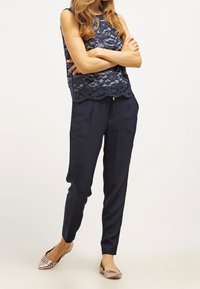 Haut sans manches en dentelle bleu marine avec ourlet festonné, associé à un pantalon ample bleu marine et des ballerines nude à motifs. Tissu lisse, look décontracté.
