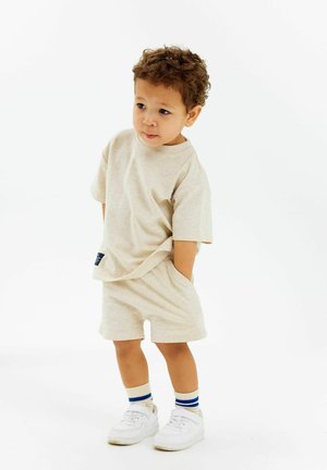 Beige bomulds t-shirt og shorts sæt med en afslappet pasform. Har korte ærmer, rund halsudskæring og et lille accentmærke. Kombineret med hvide sneakers og stribede sokker.