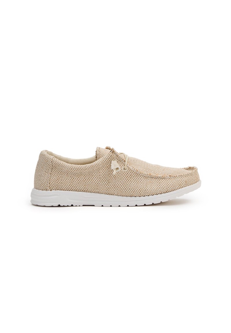 Zapato slip-on de malla beige con parte superior de tela texturizada, suela de goma blanca y detalles mínimos alrededor del área de los cordones para un ajuste seguro.