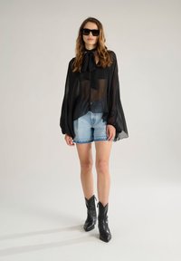 Sheer black blouse with bow tie, paired with light denim shorts featuring a frayed hem, and black ankle boots with pointed toes.