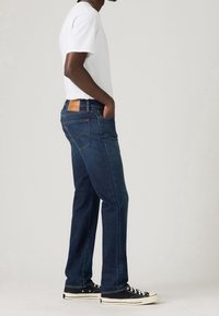 Mörkblå jeans i denim med rak skärning, utrustade med en brun läderlapp baktill. Matchade med en enkel vit t-shirt och svarta sneakers.