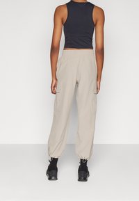 Pantaloni cargo beige con polsini elasticizzati e vita elastica, dotati di tasche laterali. Abbinati a un top aderente nero e sneakers.