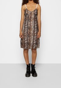Hnědá šaty se vzorem hadí kůže, tenké ramínka, délka ke kolenům, jemná textura a diskrétní logo detail na lemu. V kombinaci s černými bojovými botami.