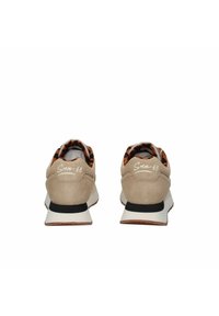 Beżowe zamszowe sneakersy z pomarańczowym wnętrzem w wzory, białą podeszwą, czarnymi akcentami i detalem logo na pięcie.