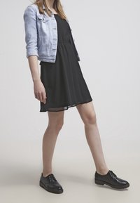 Musta ilmanhiha dressi yhdistettynä vaalean denim-takkiin ja mustiin nauhakengiin. Sileä kangas, jossa on uivan muotoinen leikkaus ja polvipituinen helma.