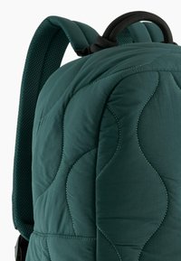 Zaino verde trapuntato con superficie testurizzata, motivi di cucitura curvi, spallacci imbottiti e manico nero a contrasto.