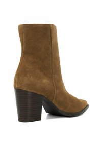 Bottine en suède marron avec un talon carré. Présente un design élégant et une pointe rétrécie. Coutures discrètes le long des coutures et talon texturé.