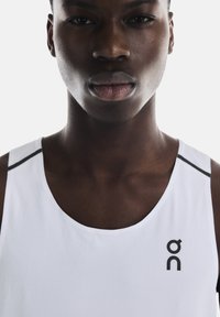 Hvid atletisk tanktop med tekstureret stof, med rund halsudskæring og sorte accenter på skuldrene, prydet med et logo.