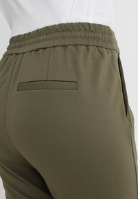 Olivgrüne Jogginghosen aus weichem Stoff, mit elastischem Bund und einer einzelnen Gesäßtasche mit rechteckigem Klappdetail.