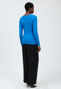 Maglione blu a maniche lunghe con collo rotondo e orlo a coste. Abbinato a pantaloni neri a gamba larga e scarpe nere con tacco.