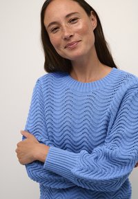 Světle modrý pletený svetr s vlnovým vzorem, žebrovaným výstřihem a manžetami, měkkou texturou a uvolněným střihem.