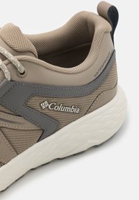 Beige och grå vattentålig sneaker med en texturerad mesh-ovandel, vadderad krage och en tjock vit sula med ett mönstrat grepp.