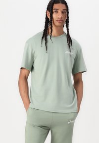 T-shirt in cotone verde chiaro con maniche corte e colletto girocollo. Caratterizzato da un piccolo logo bianco sul lato sinistro del petto. Abbinato a pantaloni jogger coordinati.