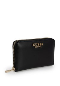 Portafoglio in pelle nera con chiusura a zip, dotato di hardware dorato e logo impresso "GUESS" con la dicitura "EST 1981". Texture liscia, forma rettangolare.