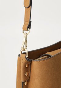 Brown suede handbag with a structured shape, accented by gold hardware, a zippered interior, and contrasting black edging.
