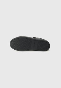 Semelle d'une chaussure noire Calvin Klein avec un motif sur la bande de roulement et le nom de la marque embossé au centre, montrée sur un fond clair uni.