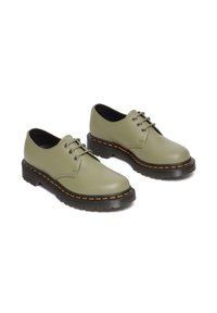 Scarpe in pelle verde oliva con punte rotonde, suole nere e una piattaforma. Presentano lacci neri e cuciture gialle lungo il bordo della suola.