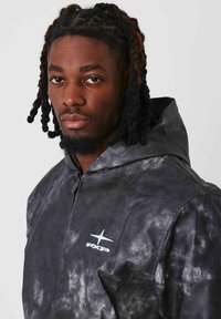 Giacca con cappuccio in un motivo tie-dye nero e grigio, con zip anteriore, texture liscia e logo bianco sul petto.