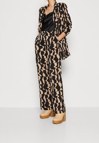 Mönstrad blus och vida byxor i svart och beige med abstrakta former. Inkluderar plattformsskor med träblockklack.