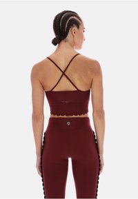 Bordo top do ćwiczeń z falbaniastym dołem, z krzyżującymi się ramiączkami. W zestawie z bordowymi legginsami, zdobionymi pomponami.