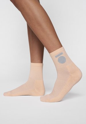 Beige ankle socks with ribbed texture, featuring a gray circular accent at the upper side, designed for comfort and fit.