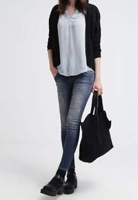 Světlomodrý top s krátkým rukávem a detailem u výstřihu, zkombinovaný s tmavými skinny džíny a černými robustními sandály. Modelka drží černou tašku.