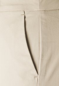 Beige maßgeschneiderte Hose mit strukturiertem Stoff, dezentem Falten-Detail und glattem Bund für eine figurbetonte Passform.