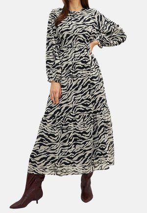 Femme portant une robe longue à manches longues, imprimé zèbre noir et blanc, longueur jusqu'aux chevilles, avec une taille froncée, associée à des bottines marron à talons et bouts pointus.